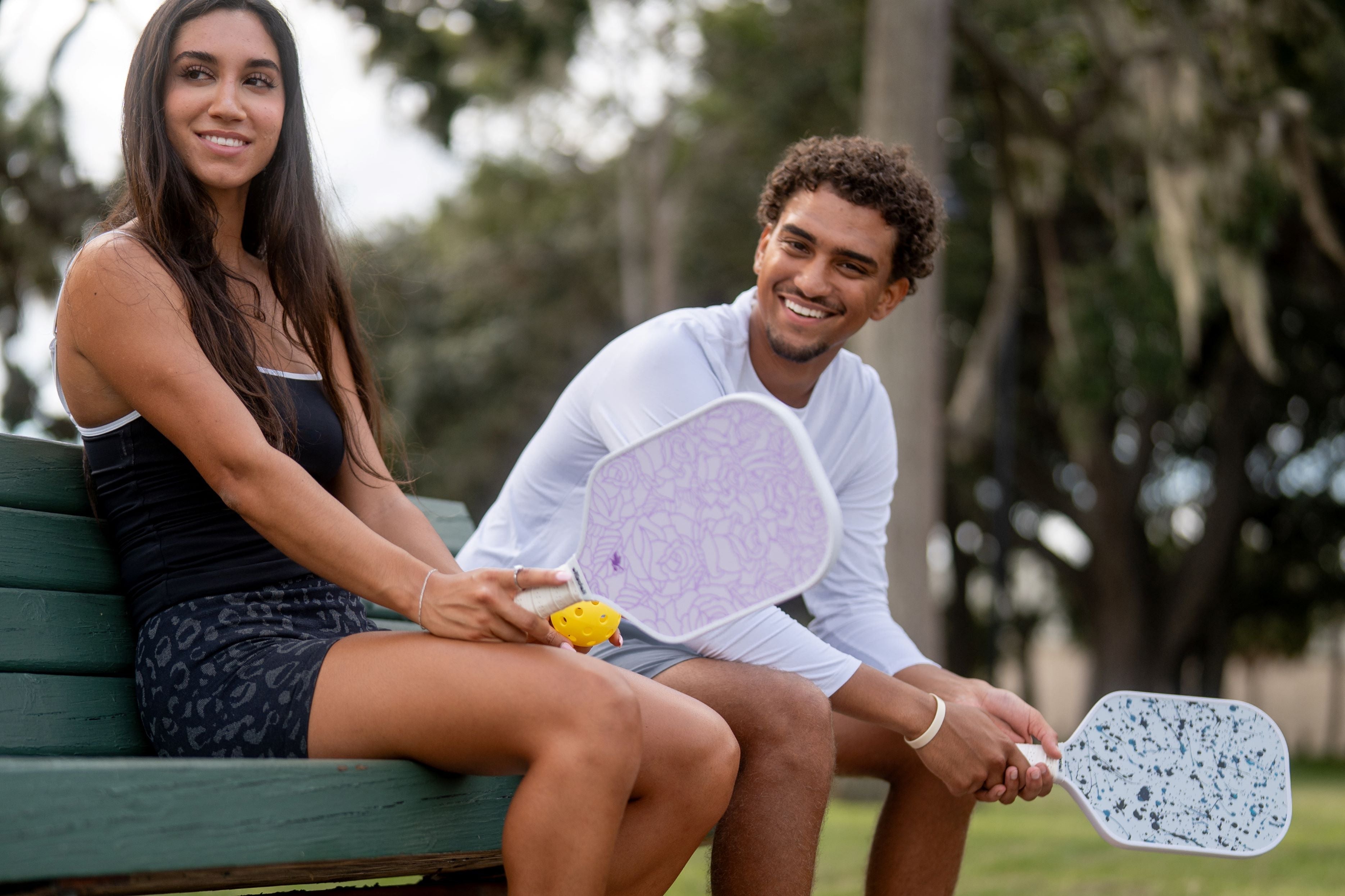 Two people sitting on a bench outdoors, holding pickleball paddles