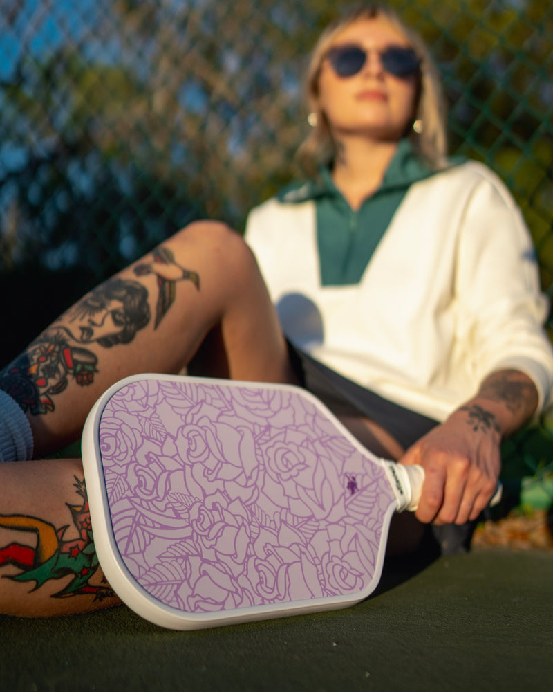 Person holding a purple pickleball paddle with a blurred background