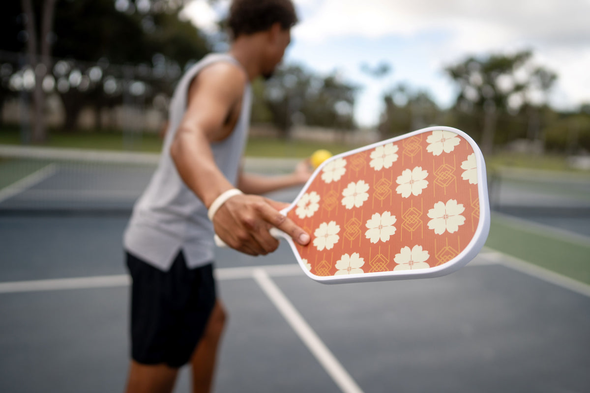 Person holding a Red floral-patterned pickleball paddle on a court.
