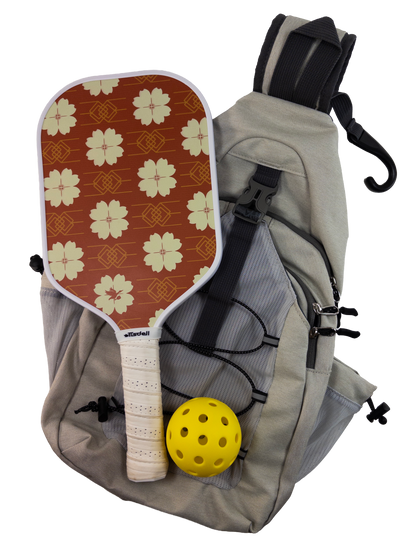 Pickleball paddle with red floral pattern, yellow ball, and gray backpack on a white background