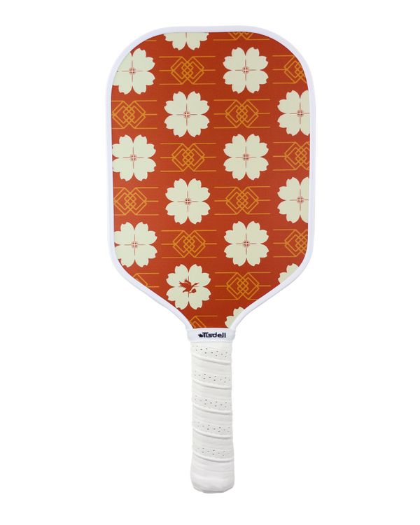 Front view of a carbon-fiber pickleball paddle with yellow / white flowers on a red background. 
