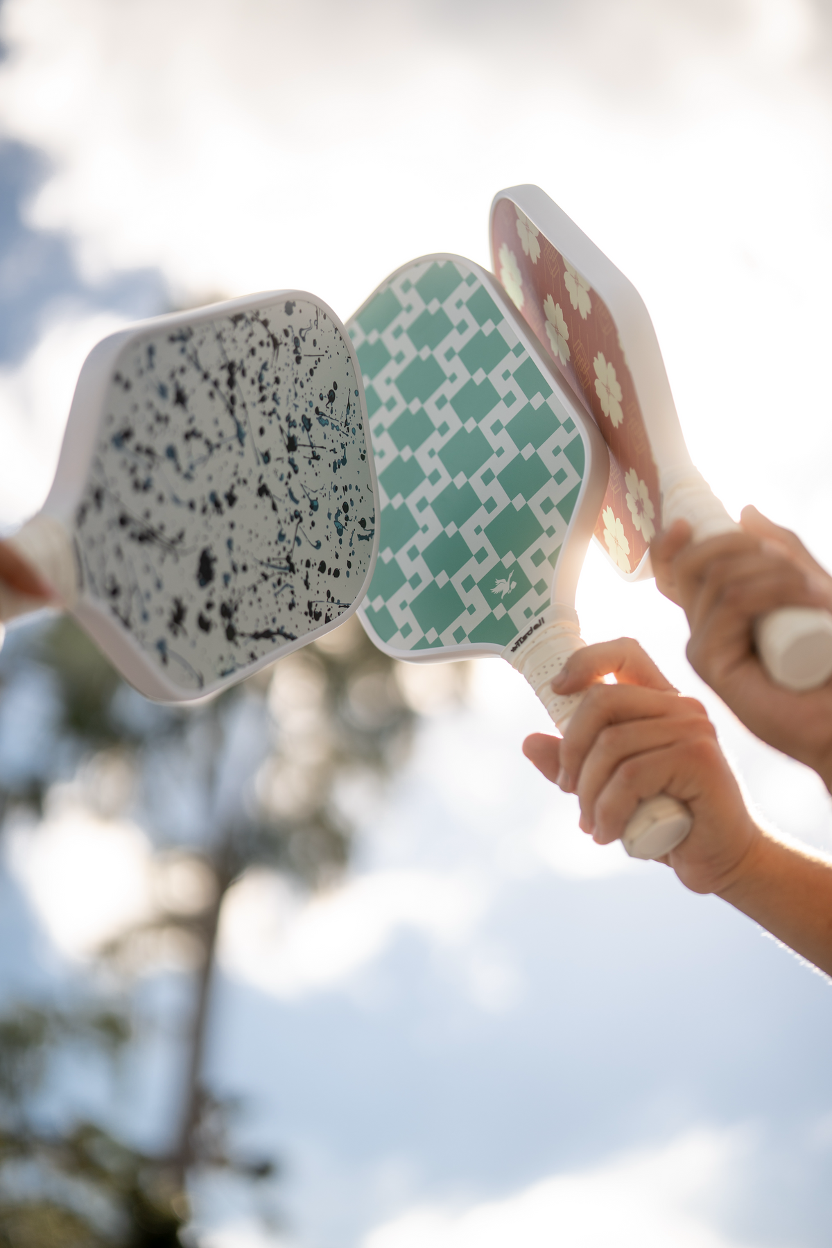 Three colorful pickleball paddles held by people against a blurred natural background